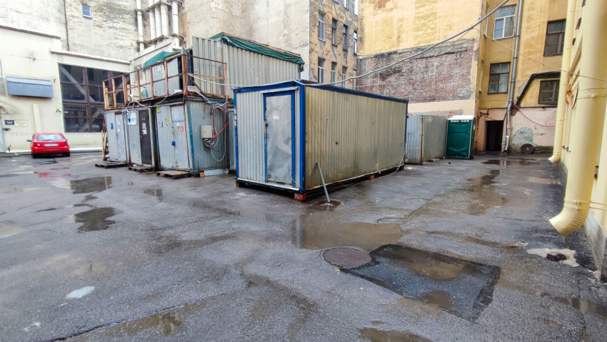 Внутридворовая площадка с металлическими бытовками, лужами и временным ограждением