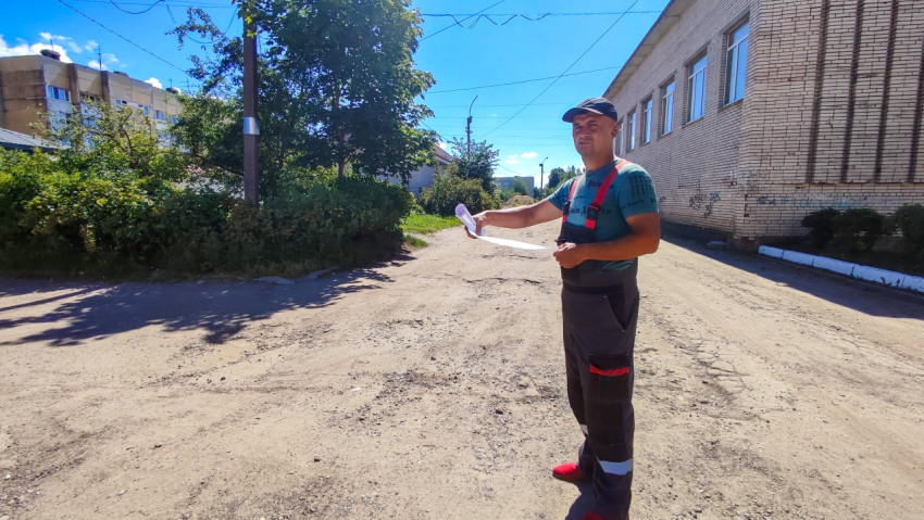 Рабочий в сигнальном жилете на грунтовой площадке у здания рядом с кустарником