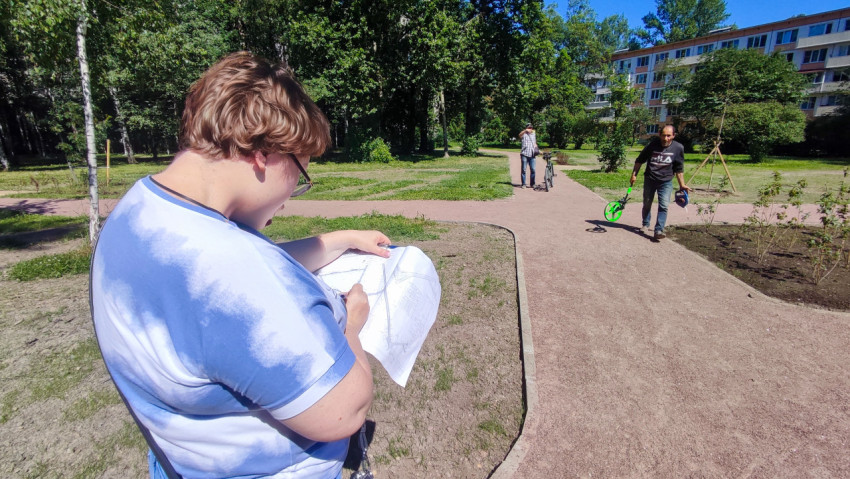 Рабочий с измерительным колесом и рулеткой проходит мимо женщины с проектными листами на пешеходной дорожке