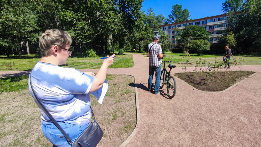 Женщина с документами указывает направление на новой пешеходной дорожке в зелёном дворе