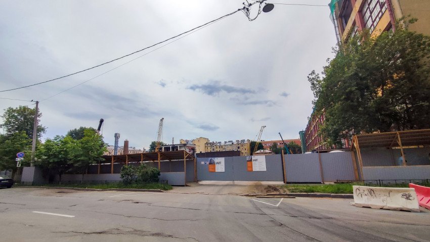 Строительная площадка за забором с паспортом объекта AVANT и строительными кранами на горизонте