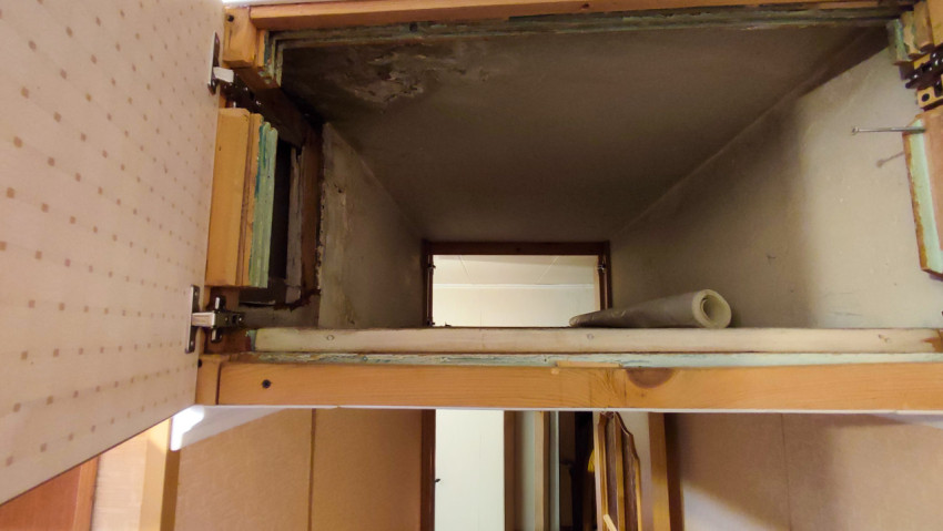 Широкий вид антресоли с открытыми дверцами и повреждённой поверхностью потолка в нише