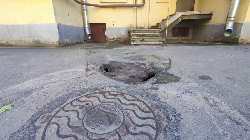 Люк на переднем плане и провал асфальта в дворовом проезде у лестницы