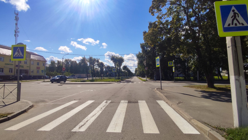 Дорожный знак «Пешеходный переход» на фоне перекрёстка и солнечного неба