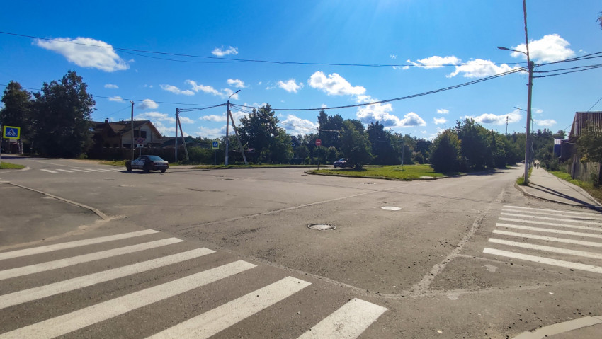 Широкий перекрёсток с разметкой пешеходных переходов, автомобилями и воздушными линиями на фоне частного сектора