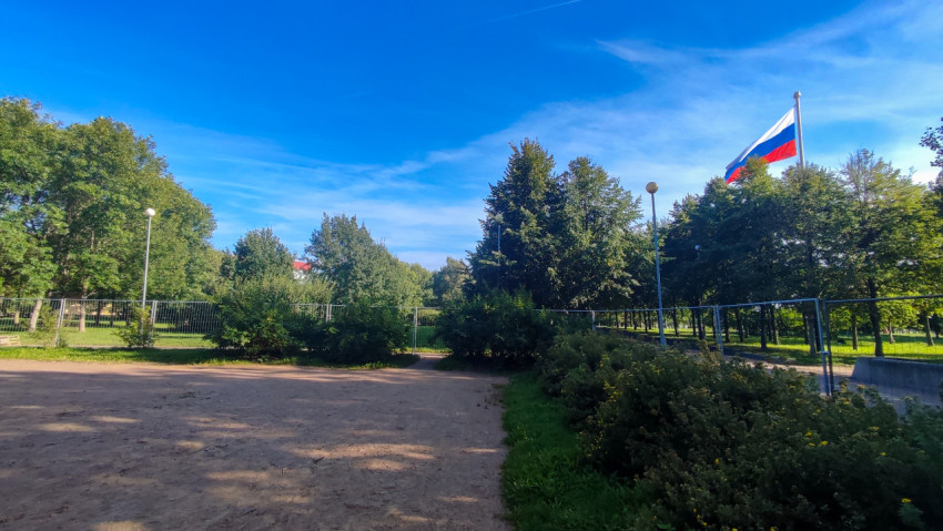 Парк с временным ограждением и флагом России на высоком флагштоке