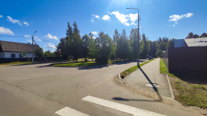 Угол перекрёстка с тротуаром у забора, люком и фонарным столбом в солнечный день