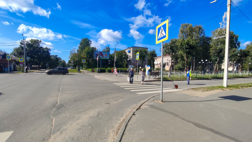Дорожный знак пешеходного перехода на фоне деревьев и неба у перекрёстка