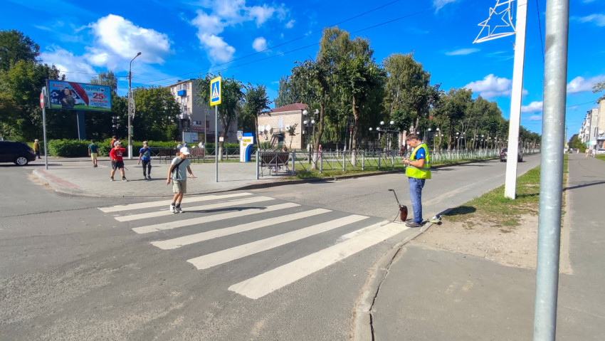 Рабочий в сигнальном жилете делает замеры у пешеходного перехода на городской улице
