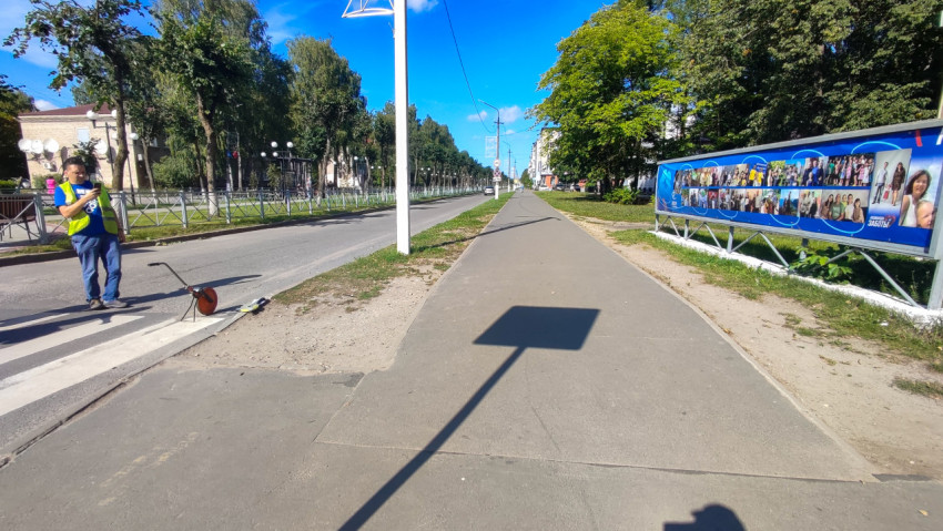 Длинная пешеходная дорожка вдоль улицы, измерительное колесо и билборд на обочине