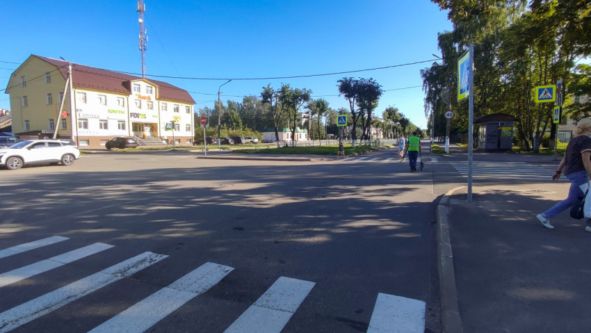 Перекрёсток с «зеброй», знаками перехода и остановкой, где дорожник уходит с измерительным колесом