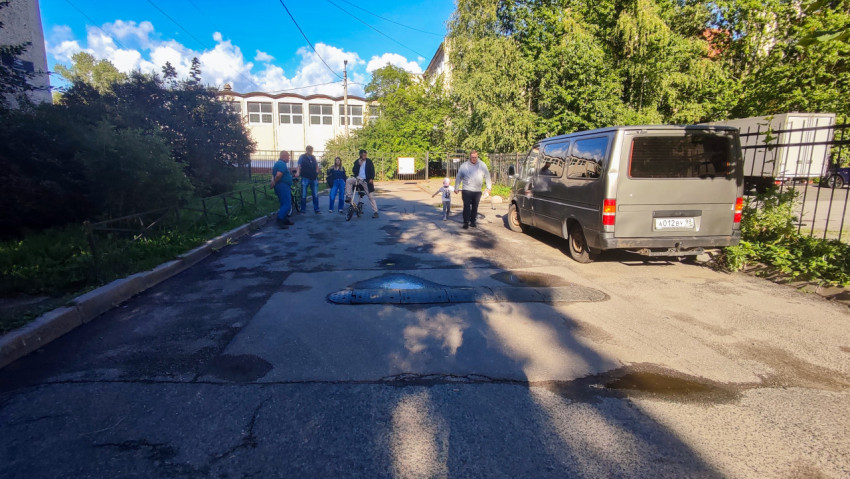 Дворовой проезд с ремонтными заплатками, лужами, припаркованными машинами и пешеходами