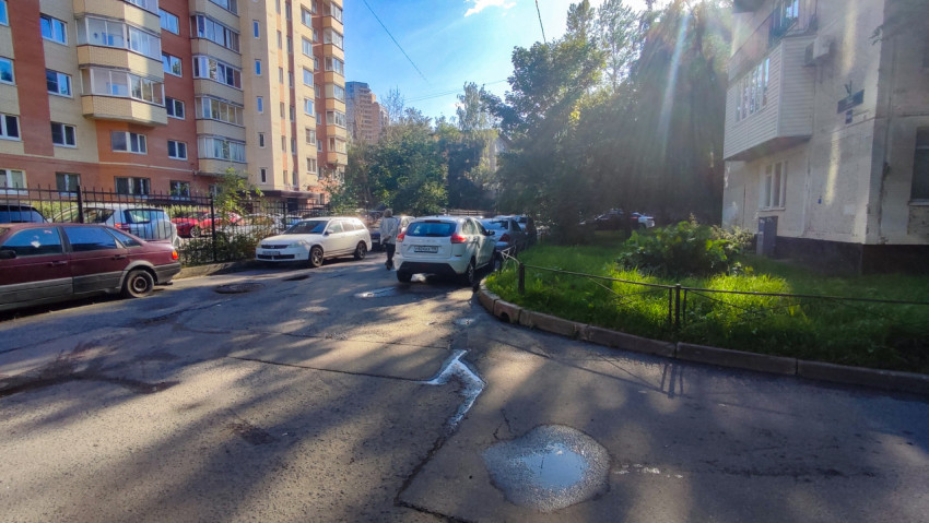 Лужи на дворовой дороге с припаркованными автомобилями и многоэтажным домом на фоне