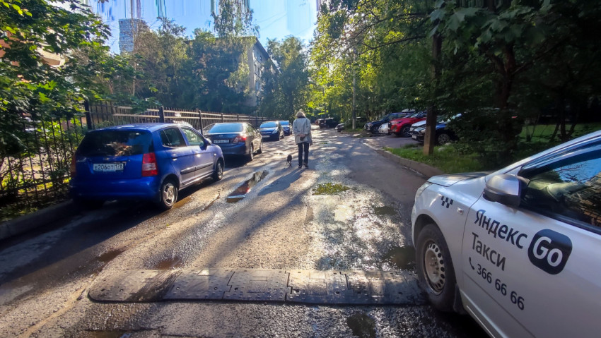 Легковой автомобиль такси Yandex Go на мокром дворовом проезде рядом с пешеходами и собакой