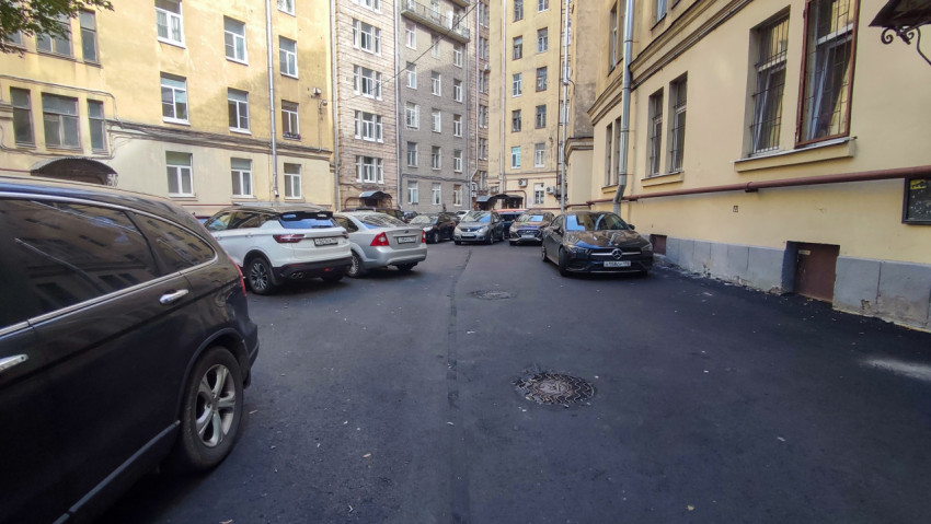 Внутренний двор старых домов с новым асфальтом, люком колодца и плотной парковкой автомобилей