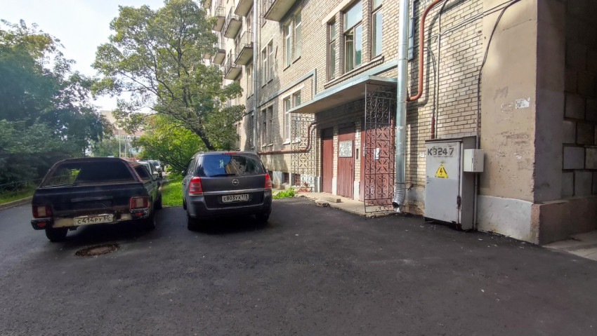 Подъездной вход в кирпичный дом с водосточной трубой, электрическим шкафом и свежим асфальтом во дворе