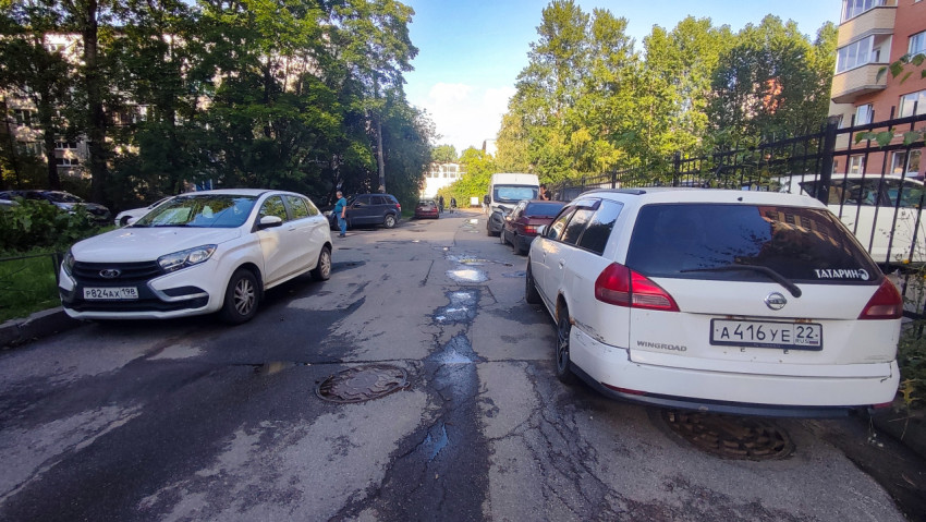 Трещины, выбоины и лужи на дворовом асфальте рядом с люком и припаркованными машинами