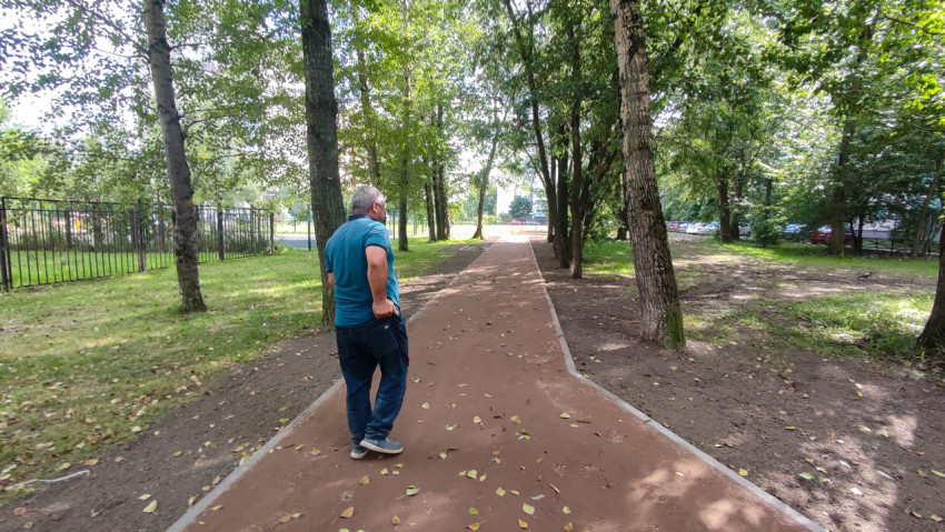 Мужчина стоит на дорожке в парке среди деревьев и зелёной обочины