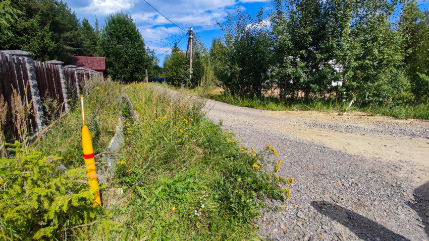 Поворот гравийной дороги в дачном посёлке с газовым маркером и линиями электропередачи