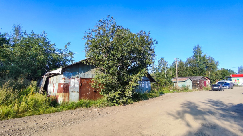 Металлический гараж с ржавыми панелями и синими дверями у проезда