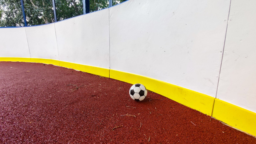 Футбольный мяч у закругленного борта дворовой спортивной коробки