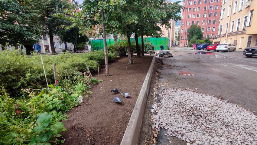 Озеленение двора с свежим грунтом, бордюром и кучей щебня на проезде