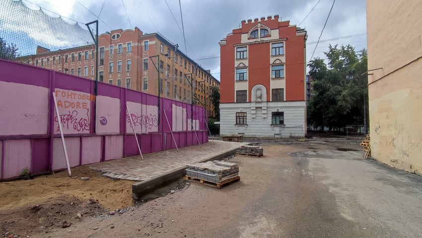 Поддоны с тротуарной плиткой у ограждения спортивной площадки на участке ремонта