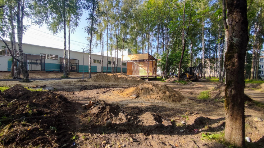 Подготовка основания под тротуар с бордюром у здания среди деревьев