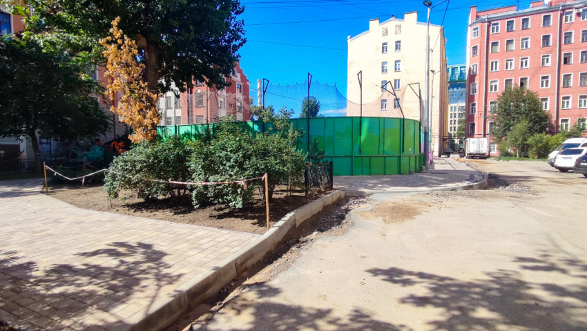 Дворовая территория со спортивной площадкой за высоким забором и новой плиточной дорожкой