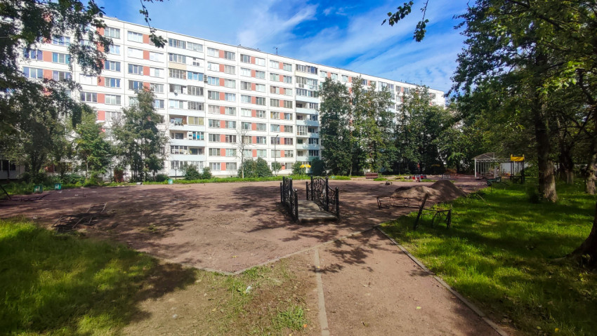 Дворовая площадка с грунтовым основанием, металлическими лавками и кучами песка на фоне многоэтажного дома