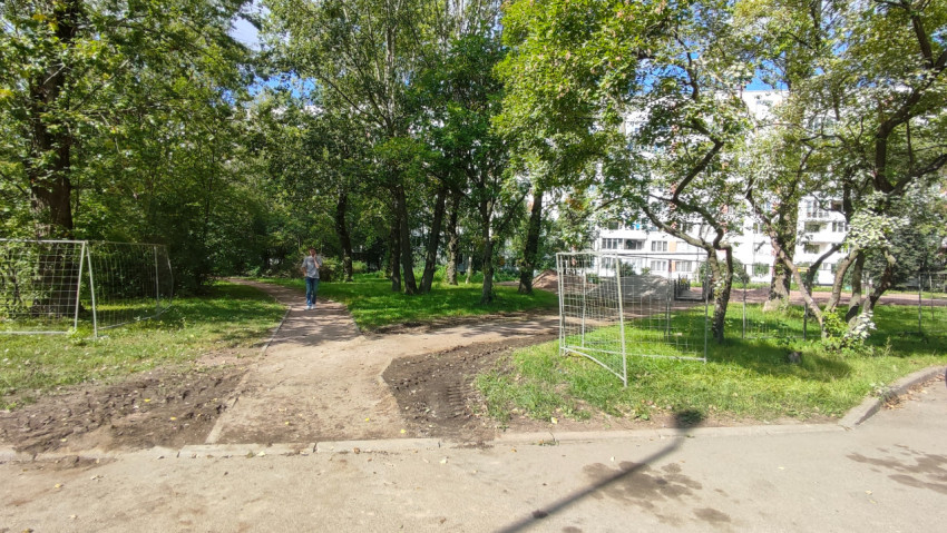 Пешеходная дорожка в зелёном дворе проходит вдоль временного строительного ограждения
