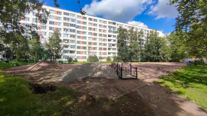 Декоративный дворовый мостик на фоне стройки и куч песка в зелёной зоне