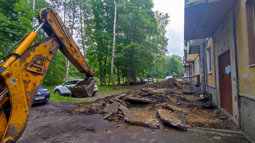 Экскаватор JCB разбирает асфальт во дворе у жилого дома