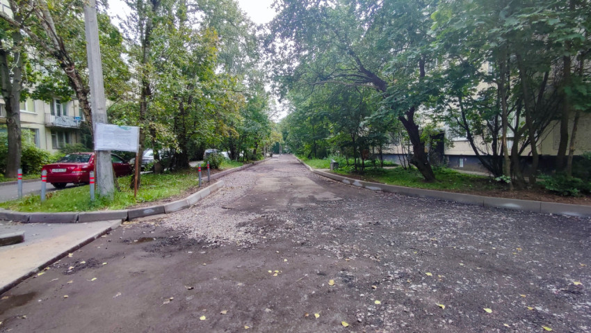 Дворовой проезд с фрезерованным асфальтом и щебнем между жилыми домами и деревьями