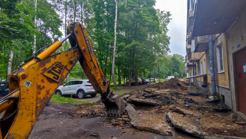 Экскаватор копает траншею рядом с тротуаром и бордюром