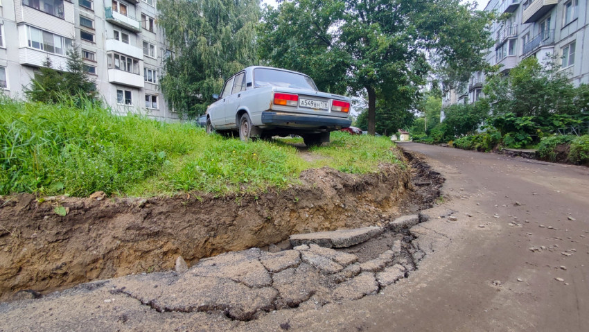 Размытая обочина и трещины на асфальте у припаркованного седана во дворе