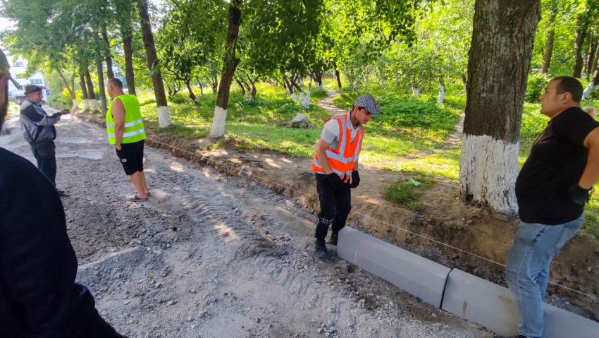 Рабочие и прораб контролируют линию бордюра на ремонтируемом проезде в зелёной зоне