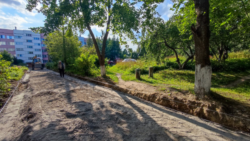Подготовка грунта и траншеи под новую дорогу во дворе, на фоне виден погрузчик и многоэтажный дом
