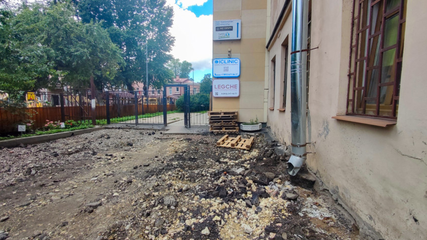 Ремонт дворового покрытия у фасада здания с металлической водосточной трубой и поддонами