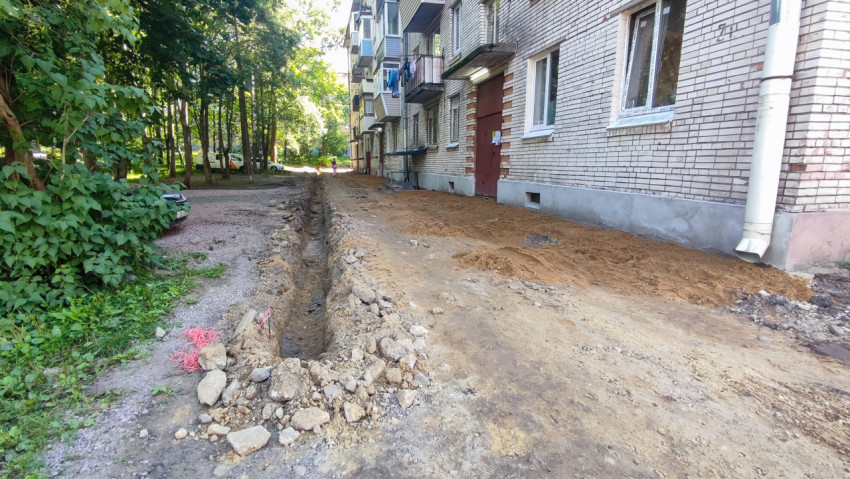 Длинная траншея и отвалы грунта во дворе у кирпичного многоквартирного дома