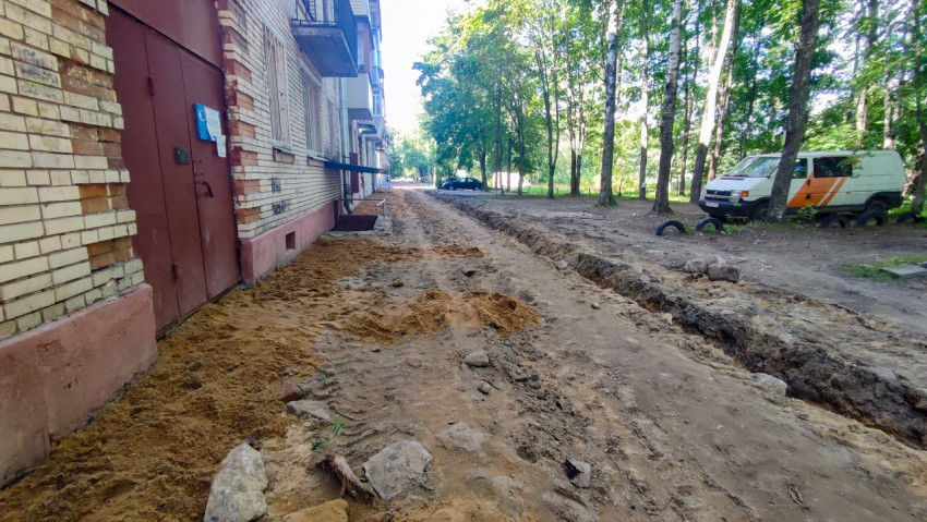 Траншея вдоль фасада с кучами песка, шинами-барьерами и припаркованным фургоном