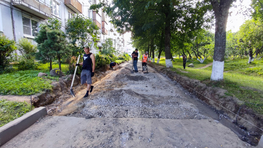 Рабочие выравнивают основание и засыпают щебень на ремонтируемой дворовой дороге у жилого дома