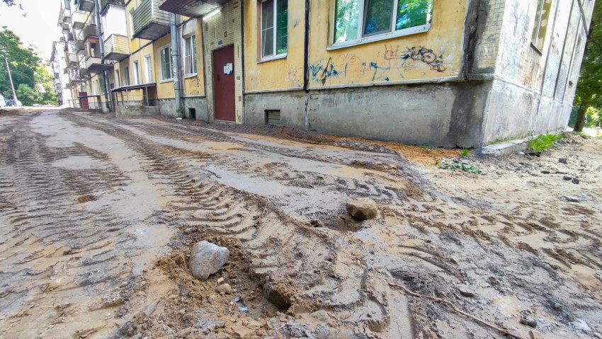 Разобранное дворовое покрытие с песком, камнями и колеями у фасадов жилых домов