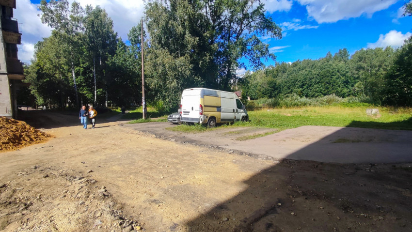 Грунтовая площадка у жилого дома с припаркованным фургоном и пешеходами