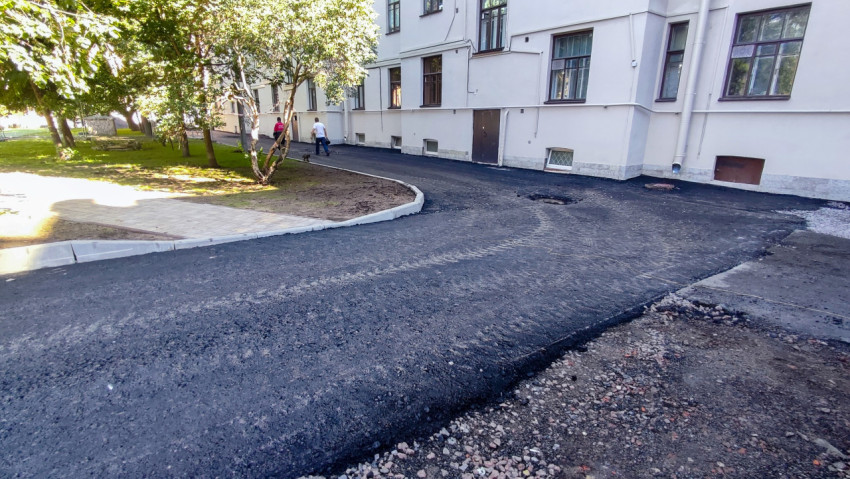 Свежий асфальт на дворовом проезде у здания с новым бордюром и тротуаром