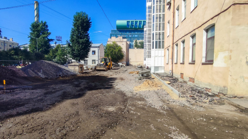 Экскаватор-погрузчик работает на площадке с кучами щебня рядом с жилыми домами