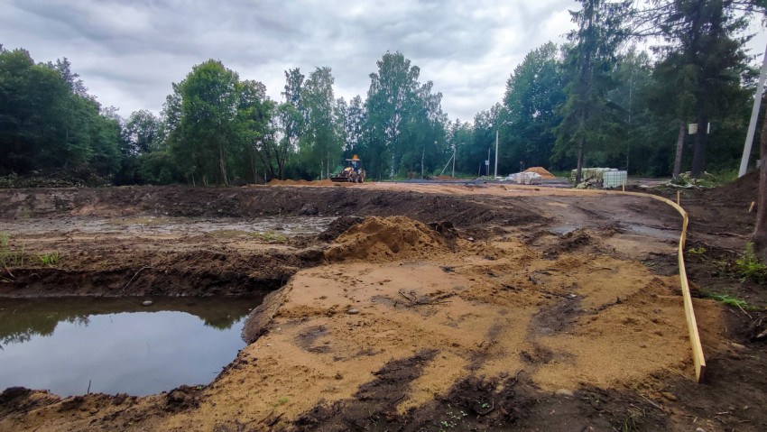 Земляные работы в лесопарке с экскаватором-погрузчиком, песком и временными ограждениями