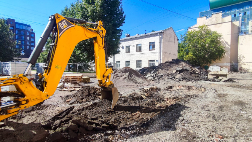 Жёлтый экскаватор CAT копает грунт среди куч щебня и строительного мусора во дворе