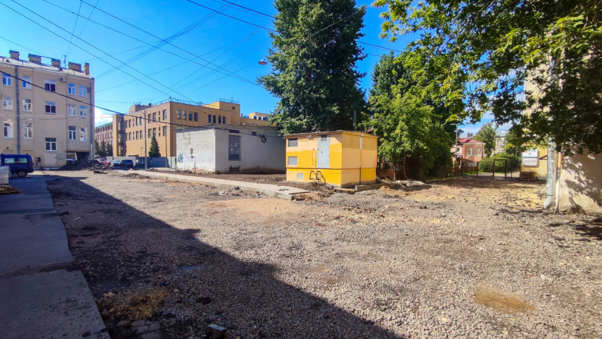 Жёлтый технический павильон на щебёночной площадке под воздушными проводами между городскими зданиями