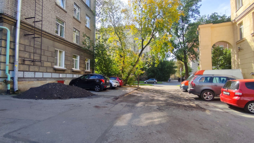 Двор-колодец с припаркованными автомобилями, кучей грунта у фасада и арочным проездом между домами